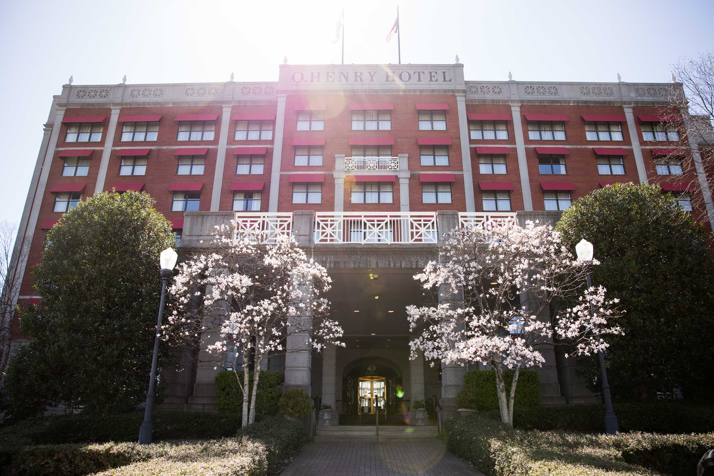 View of the front of the O.Henry Hotel with the sun shining from behind during early springtime with flowers blooming out front