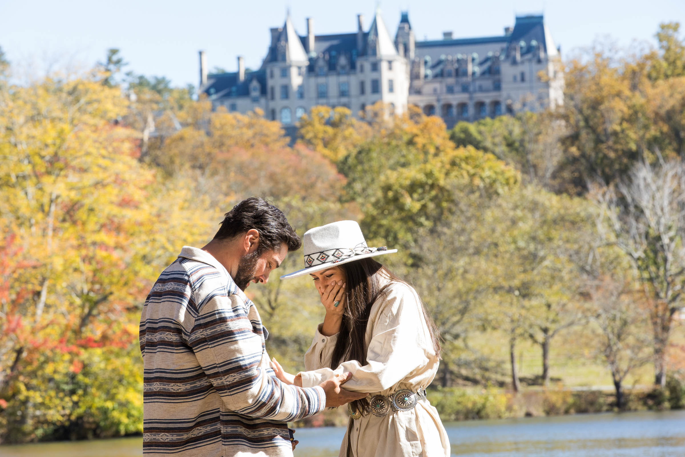 women surprised and happy looking at her fiance putting her engagement ring on her finger during their proposal at the biltmore estate