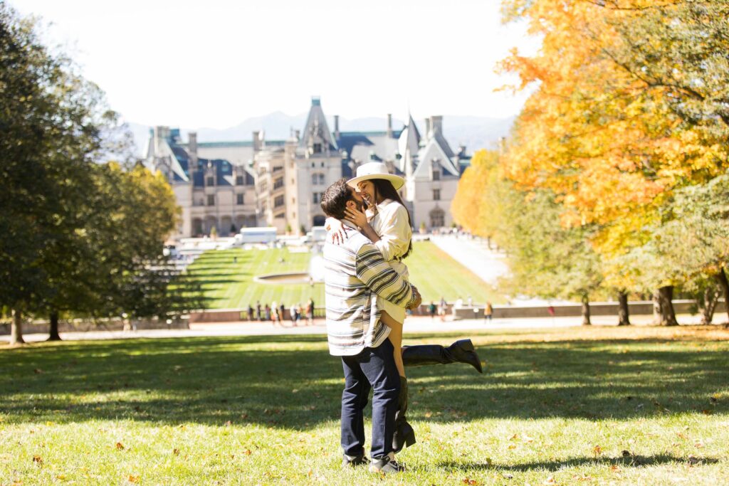 man picks up his girlfriend as they kiss on the lawn overlooking the biltmore estate in asheville after their surprise marriage proposal 