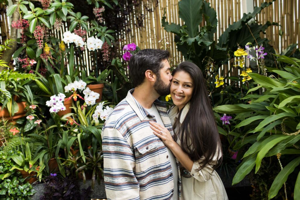 man kisses his fiancee amongst the orchids in the biltmore estate convervatory gardens