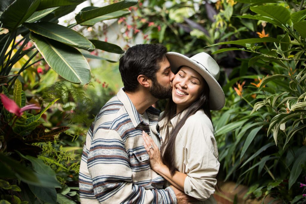 man kisses his fiancee in the conservatory surrounded by plants after their proposal at the biltmore estate