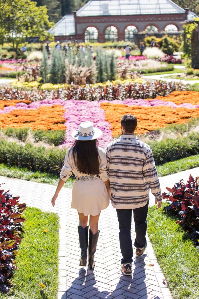 couple walks away from camera into the gardens at the biltmore estate in the fall