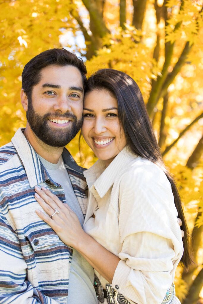 couple smiles with the yellow leaves of a maple tree at the biltmore estate in the fall after their proposal