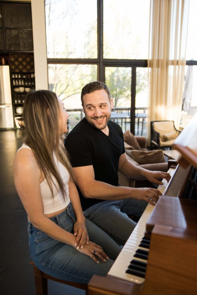 man smiles as he plays piano for his fiancee in their airbnb in the mountains of nc