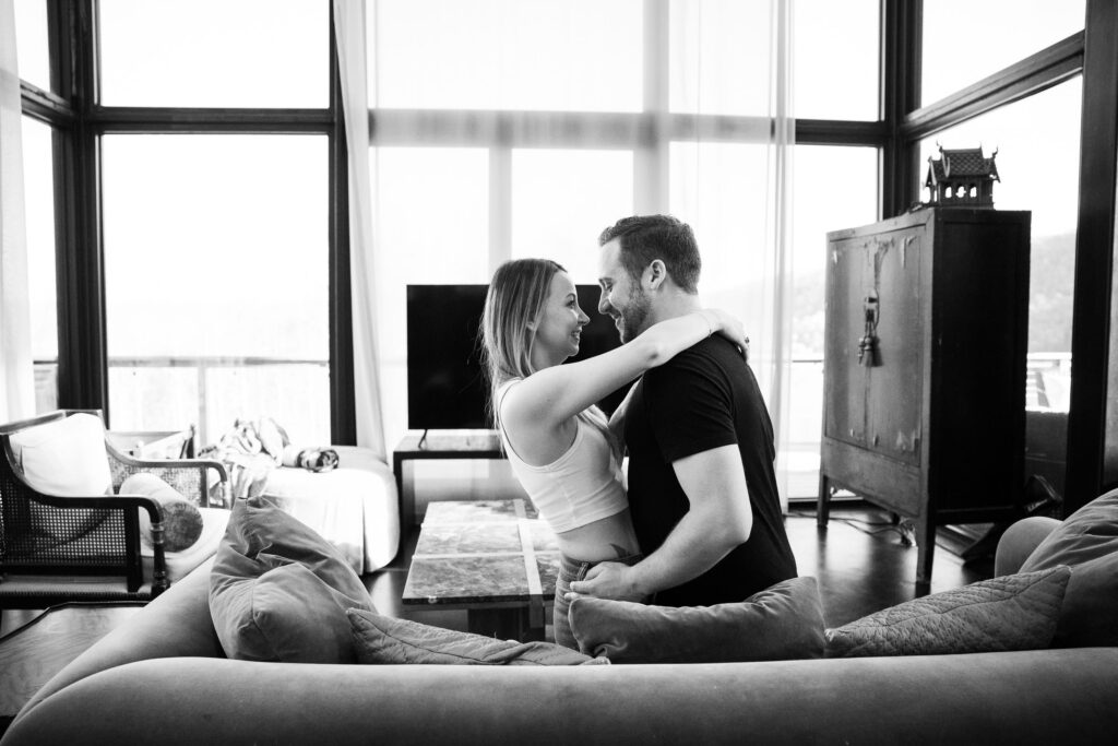 black and white photo of a couple embracing on a couch in a room full of windows