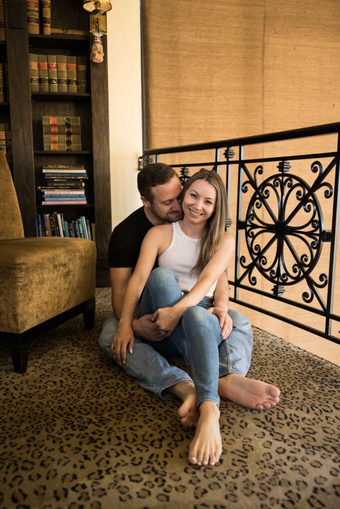 man nuzzles his fiancee while they sit barefoot on the floor of the library at the redstone mansion