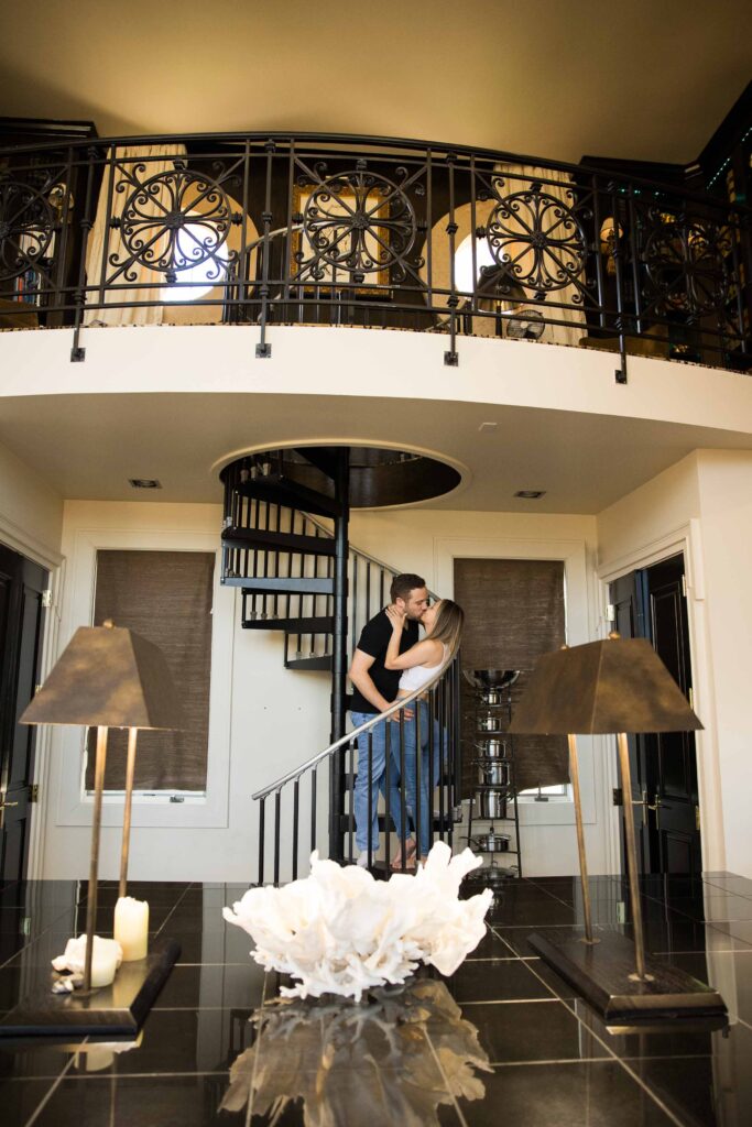 engaged couple kisses on a spiral staircase at their airbnb, the redstone mansion in burnsville