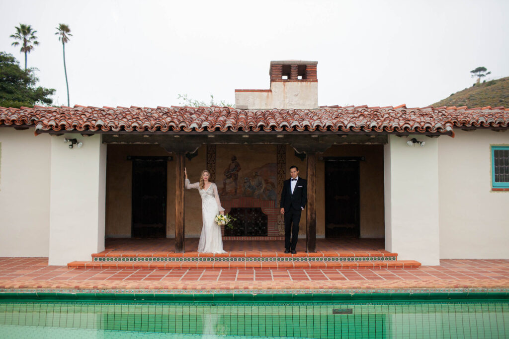 bride and groom standing next to the pool with the Malibu hills in the background at the Adamson House in California