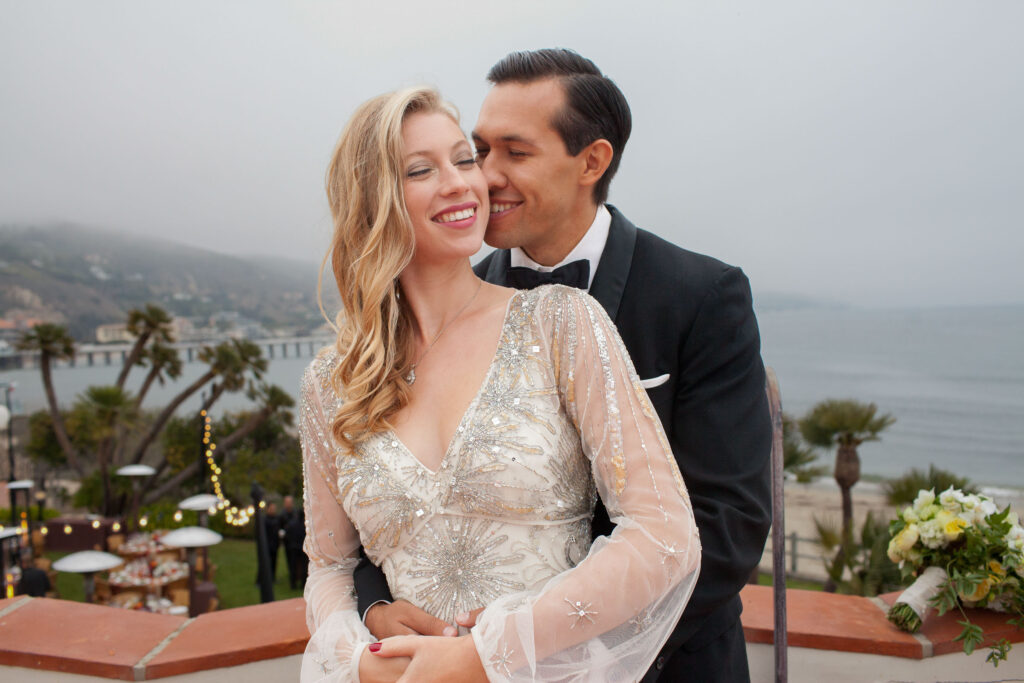 couple on the balcony of the adamson house with the ocean and malibu hills behind them