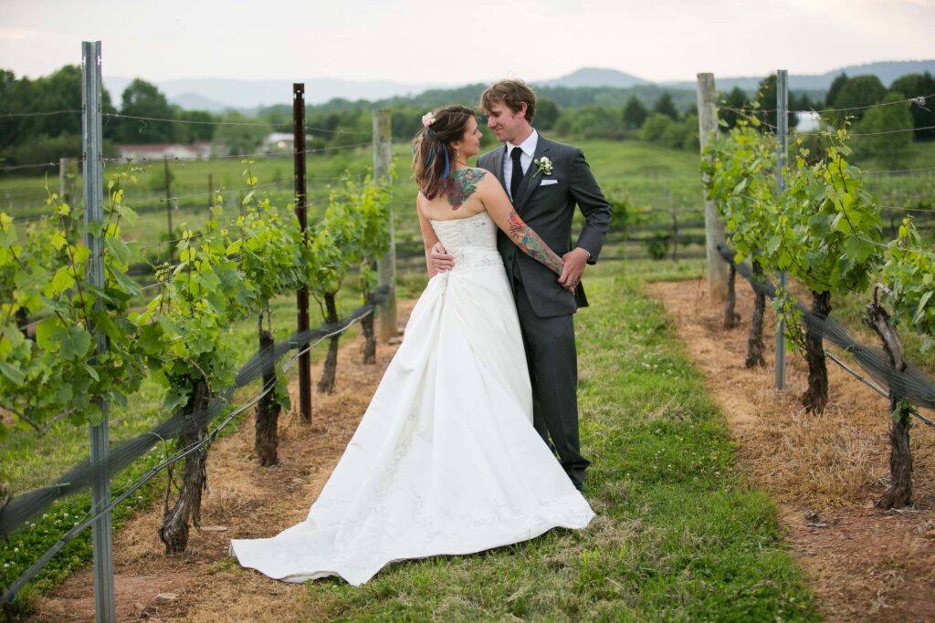 couple amongst the grapevines on their wedding day at round peak vineyard in mount airy