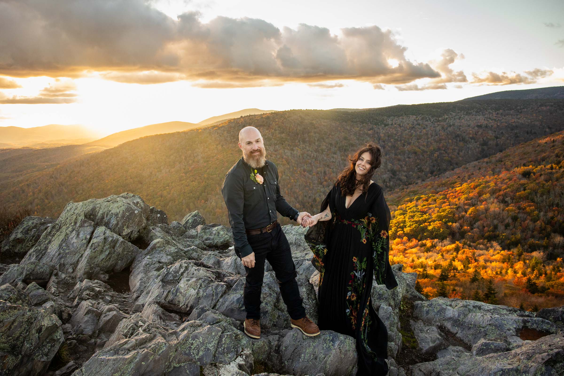 Grayson Highlands bride and groom eloping at Big Pinnacle with the sunset behind them and the fall leaves illuminated on the mountainside behind them
