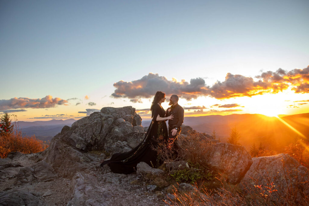 Wedding couple standing on a rocky peak with the sun setting behind them at grayson highlands state park in virginia