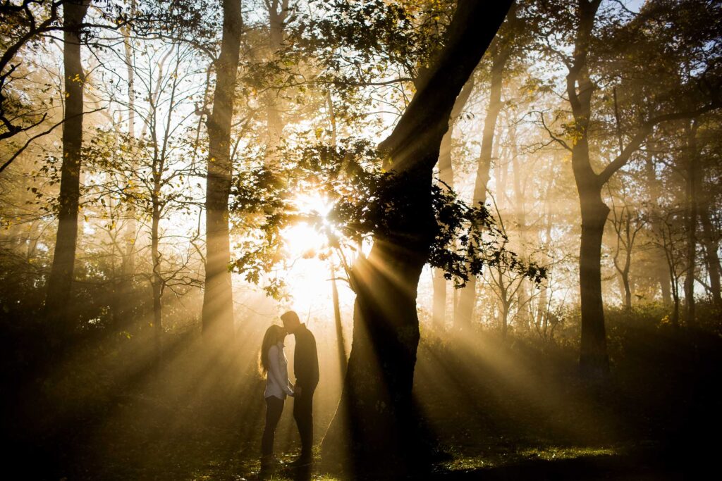 engaged couple kissing with golden light rays streaming through fog at sunrise on the blue ridge parkway
