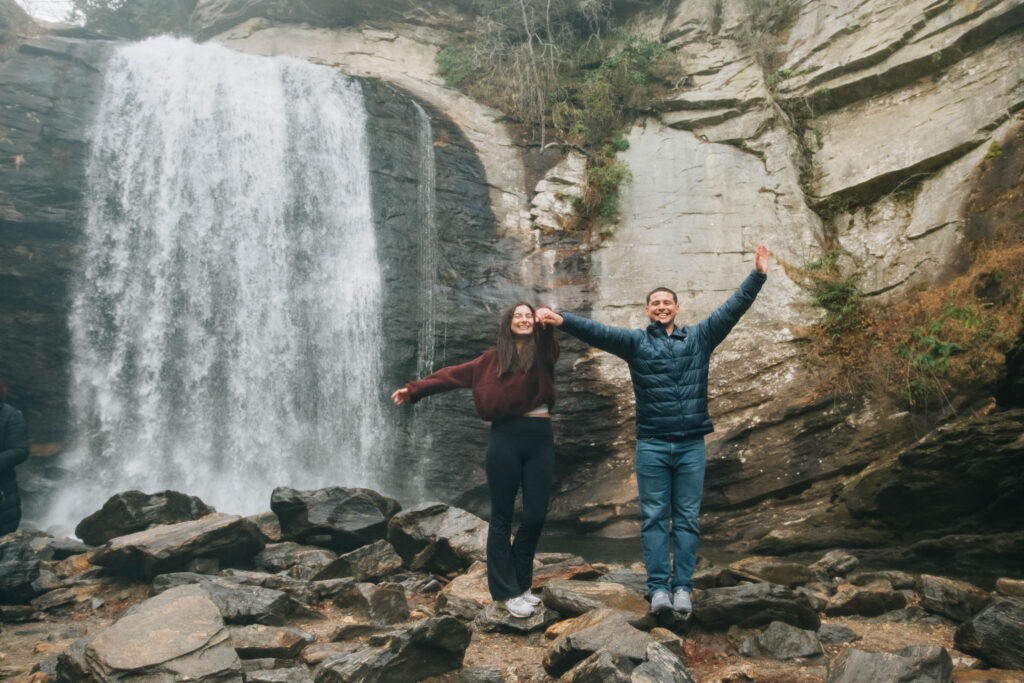 Engaged couple cheers after a surprise proposal at Looking Glass Falls near Brevard, North Carolina.