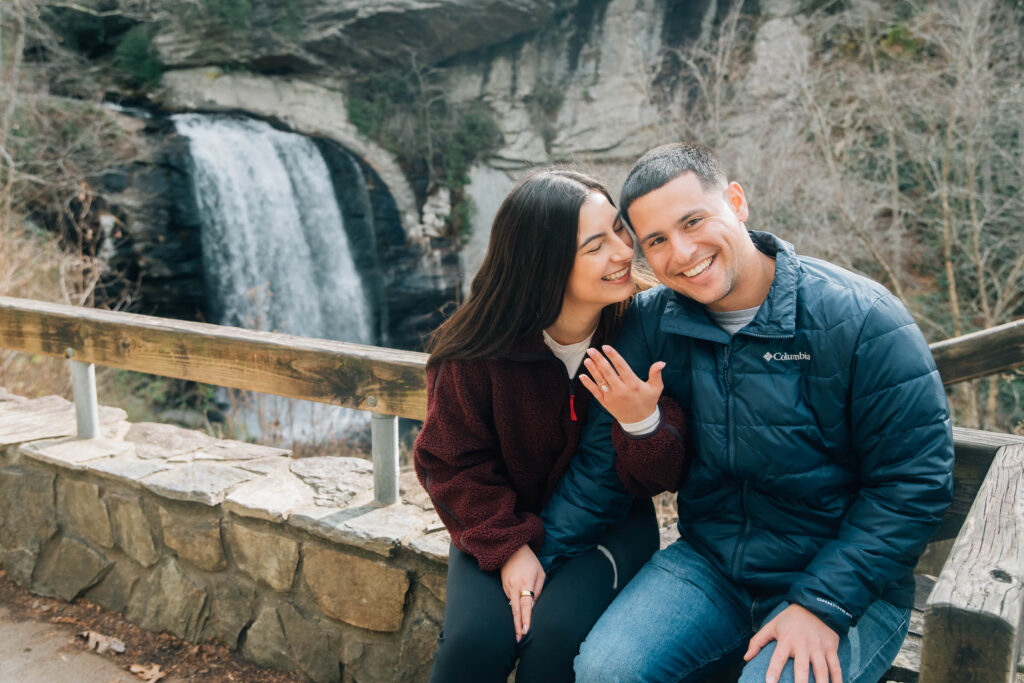 Newly engaged couple sitting together near Looking Glass Falls in Pisgah National Forest, Brevard NC, celebrating a surprise waterfall proposal.