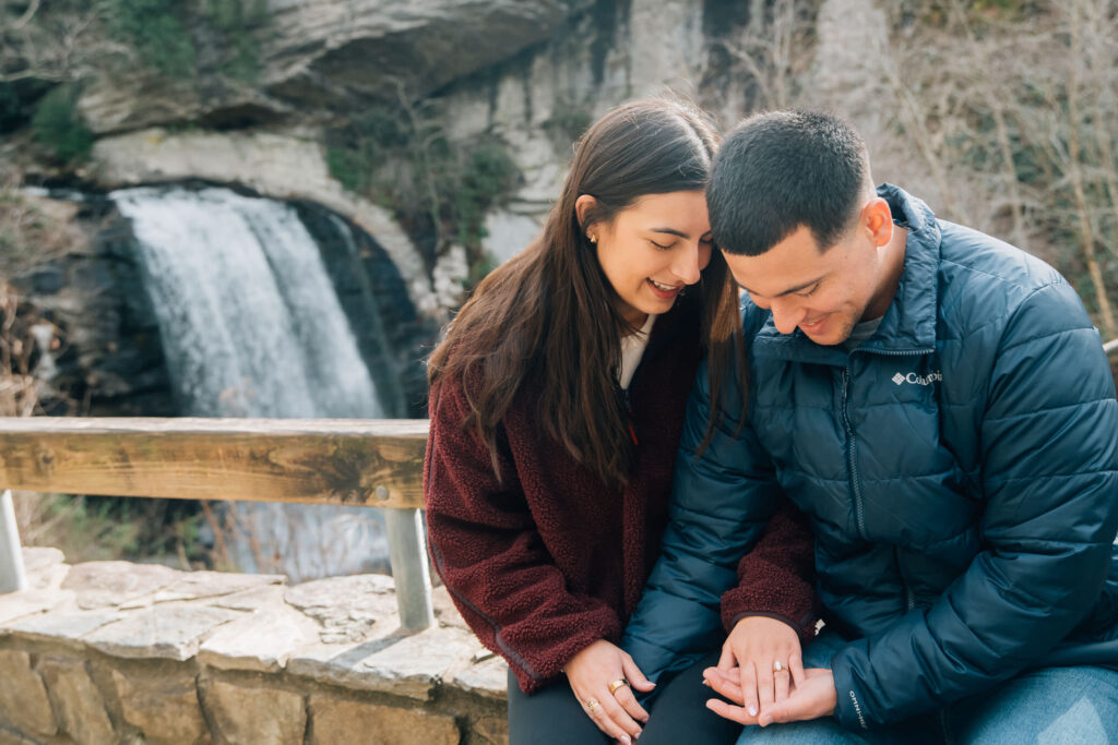 Newly engaged couple sitting together near Looking Glass Falls in Pisgah National Forest, Brevard NC, celebrating a surprise waterfall proposal.