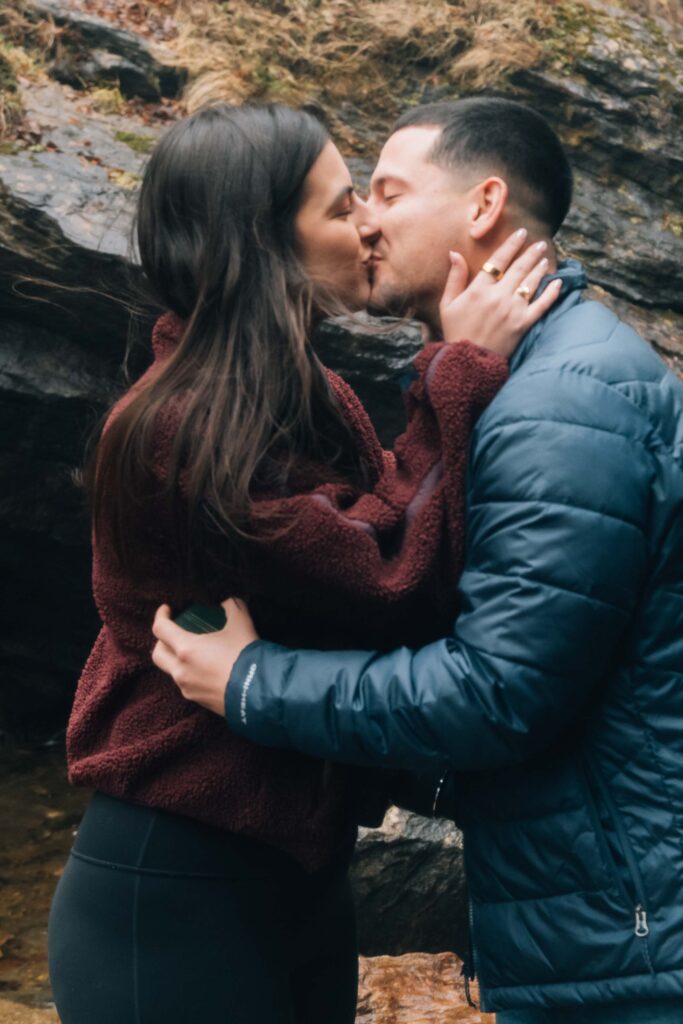 Newly engaged couple kissing near Looking Glass Falls in Pisgah National Forest, Brevard NC, celebrating a surprise waterfall proposal.