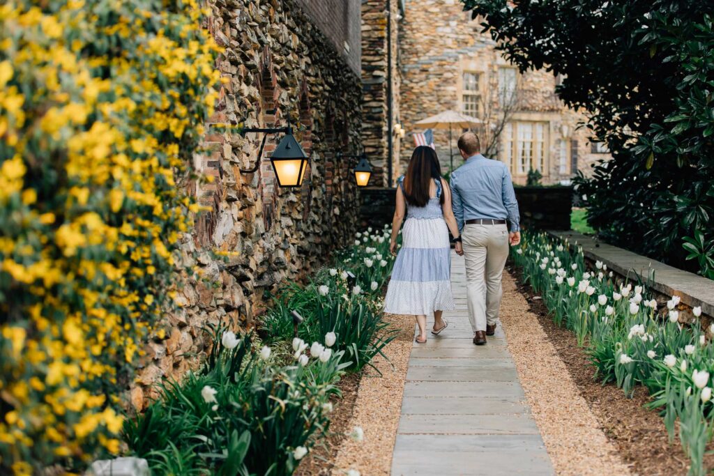 couple walks down path lined by flowers in the springtime at the graylyn estate