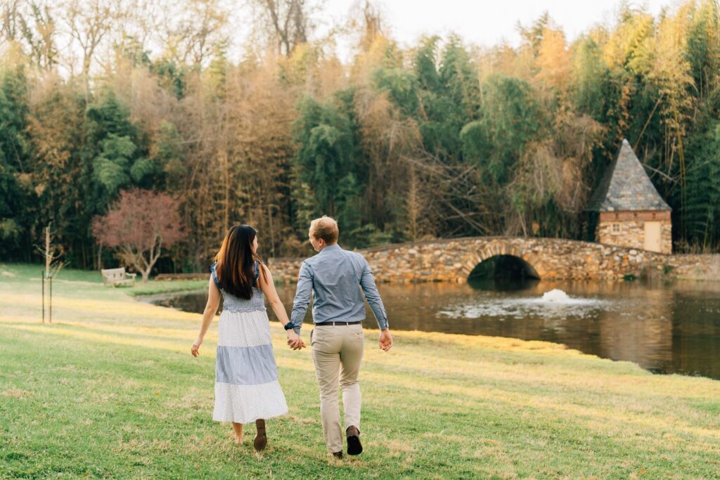 couple walks toward the stone bridge at the graylyn estate in nc