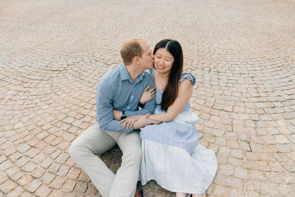 man kisses woman on the cheek while sitting on cobblestone at the mews at the graylyn estate