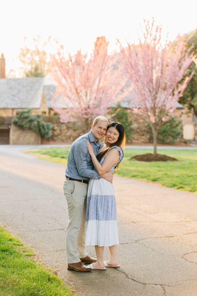 newly engaged couple smiling with red bed trees in front of the mews at the graylyn estate in winston-salem, nc