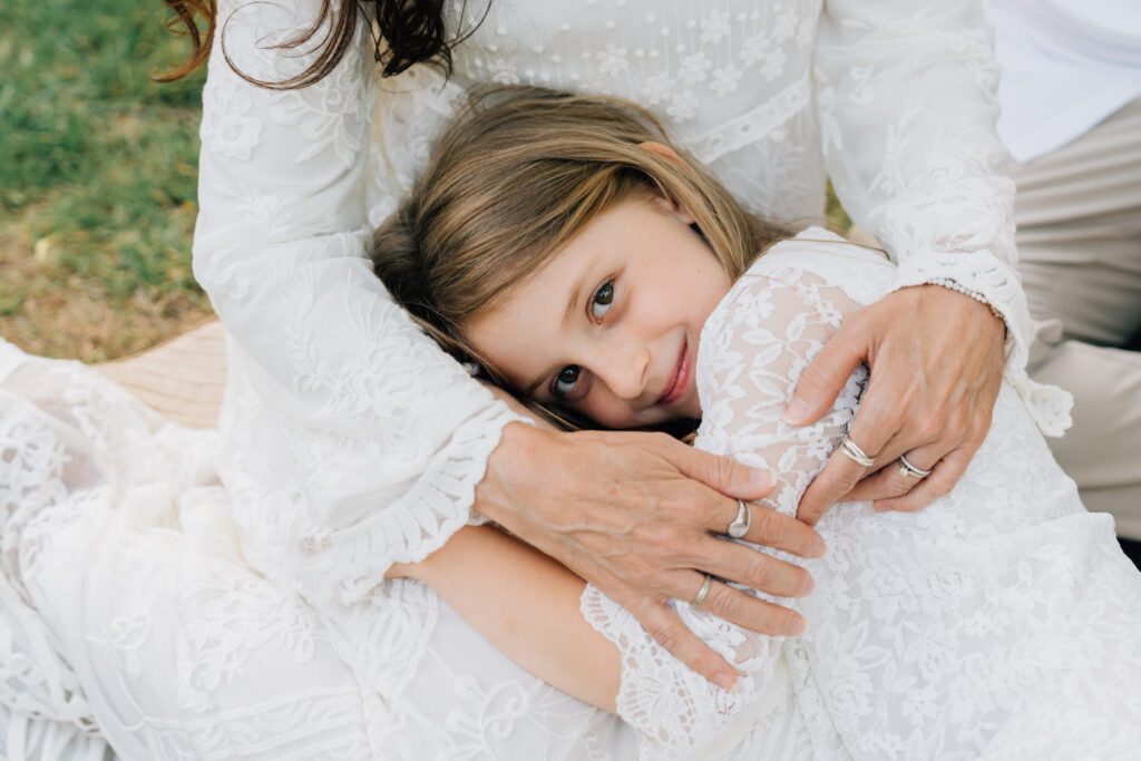 little girl in all white rests in her mother's lap with a sweet smile at hurley park in salisbury nc