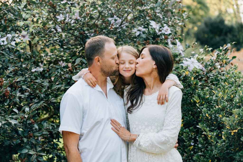mom and dad kiss their daughters cheeks as she hugs them