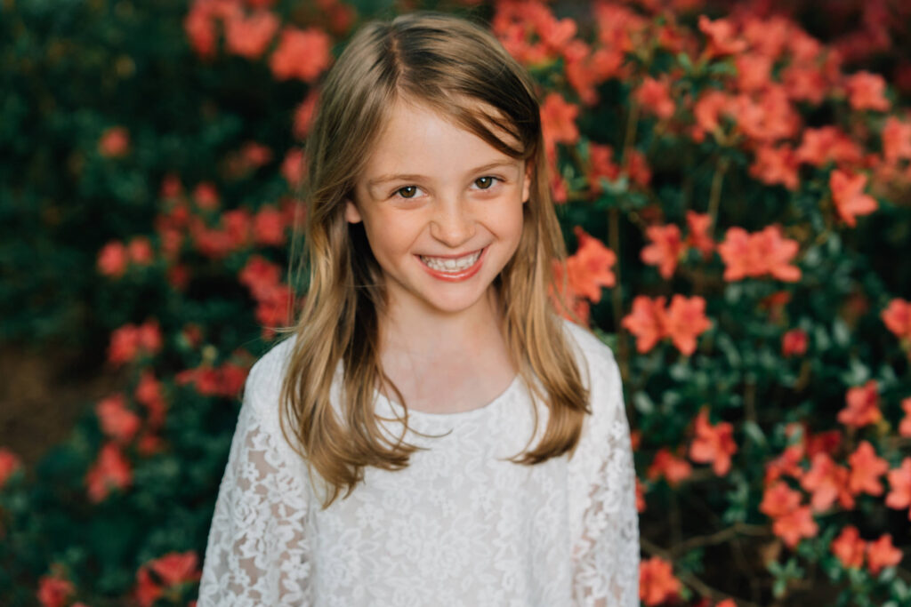 little girl grins while standing in front of red azaleas in hurley park salisbury nc