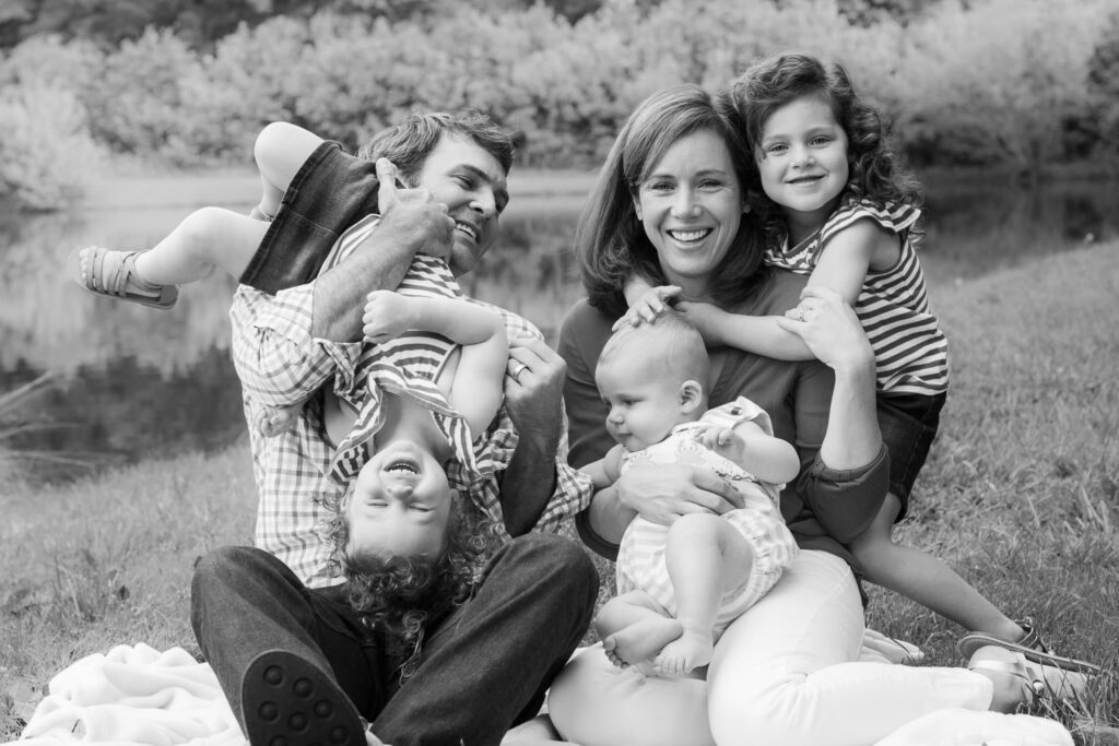 black and white photo of family sitting together with a toddler upside down, and everyone playing and cuddling
