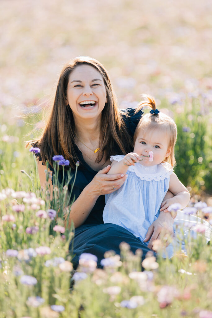 toddler smells a flower as her mom laughs at dogwood farms