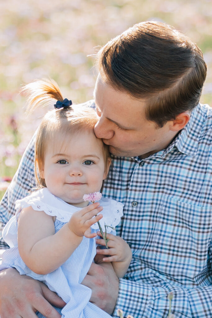 dad kisses toddler while she holds a wildflower at a flower farm in nc