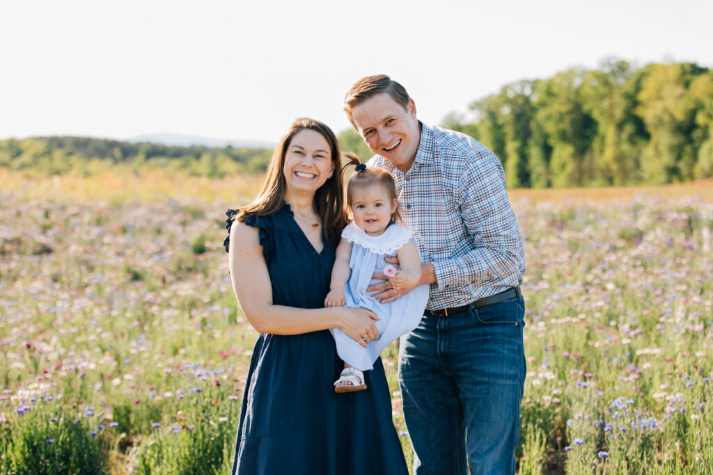 family of 3 smiles in a flower field at dogwood farms