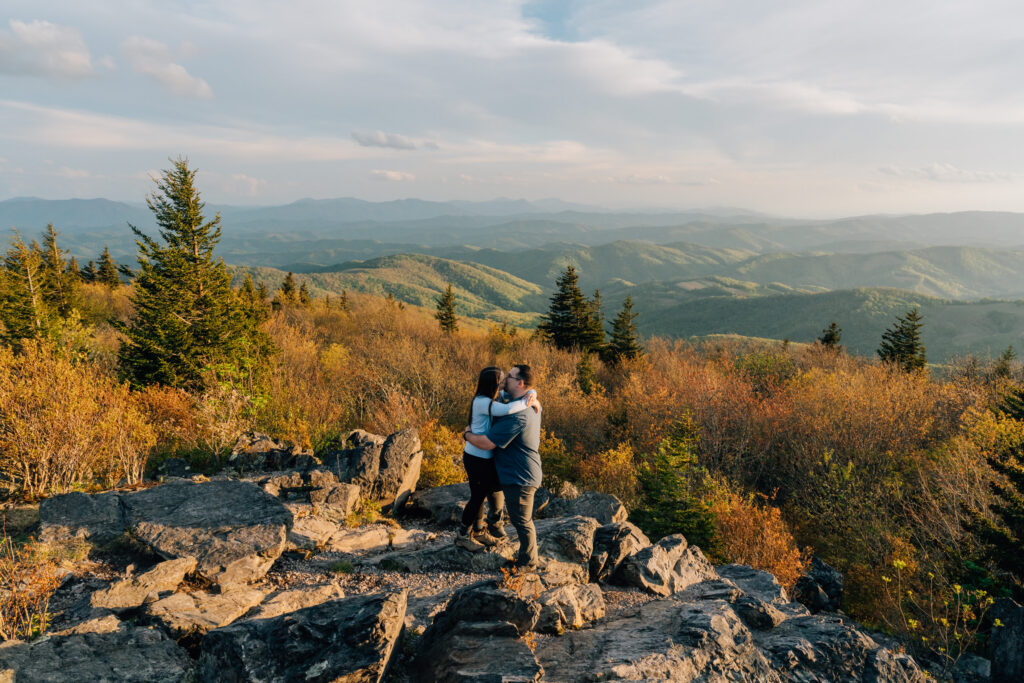couple embraces on a mountaintop with the blue ridge mountains behind them after their surprise proposal in va
