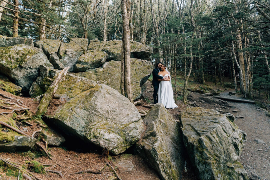 couple stands amongst huge boulders in a forest during their hiking elopement on the NC TN border