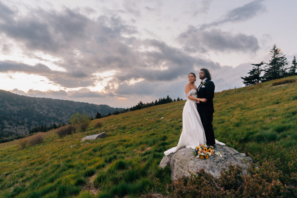 married couple stands on top of boulder during their sunset elopement at carver's gap