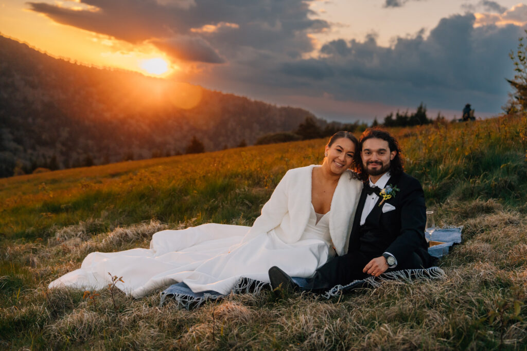couple eloping at roan mountain smiles at sunset while relaxing on a blanket