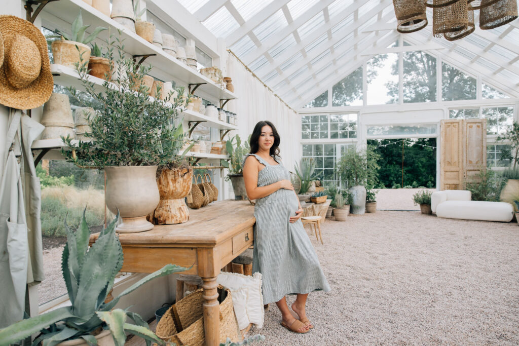 woman stands inside fleurish greenhouse during her maternity session