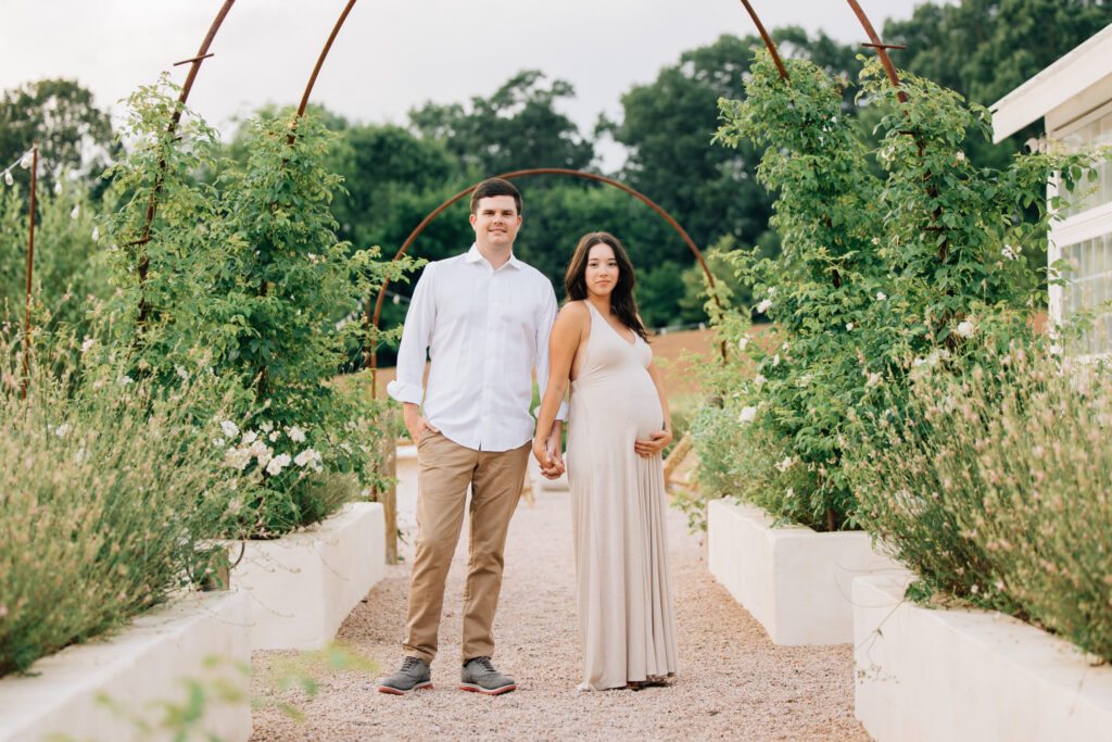couple holds hands outside fleurish greenhouse during maternity session