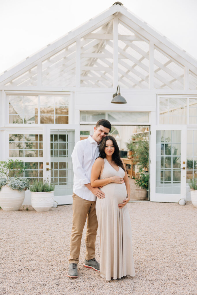 couple holds hands outside fleurish greenhouse during maternity session