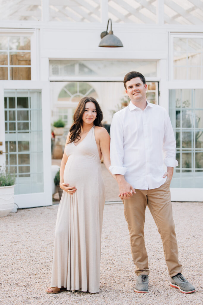 couple holds hands outside fleurish greenhouse during maternity session