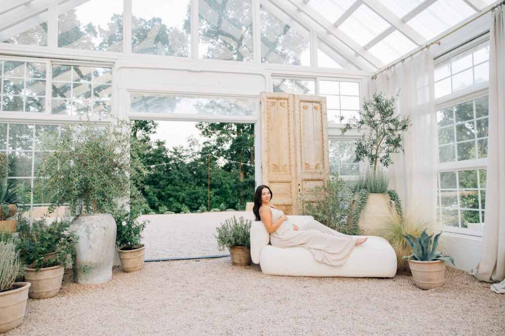 mom sits on couch during her maternity photo session at fleurish greenhouse