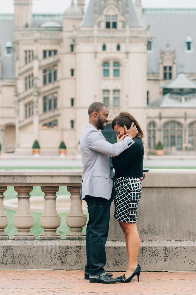 man smiles and hugs his fiancee as she cries happy tears during their proposal at the biltmore estate
