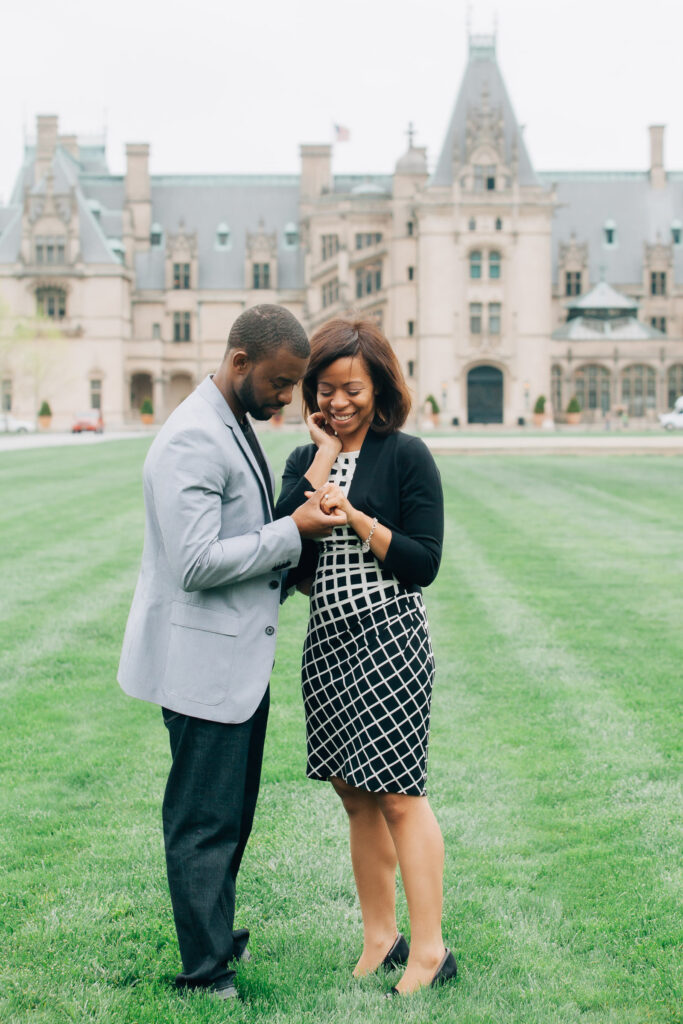couple looks at their new engagement ring on the lawn of the biltmore estate
