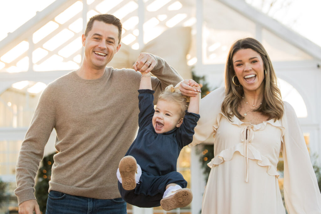 mom and dad lift toddler into the air during christmas mini session at fleurish greenhouse in taylorsville, nc