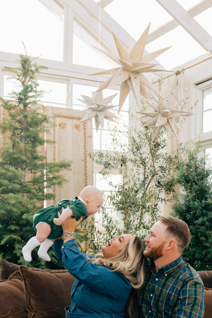 mom and dad lift baby into the air during christmas mini session at fleurish greenhouse in taylorsville, nc