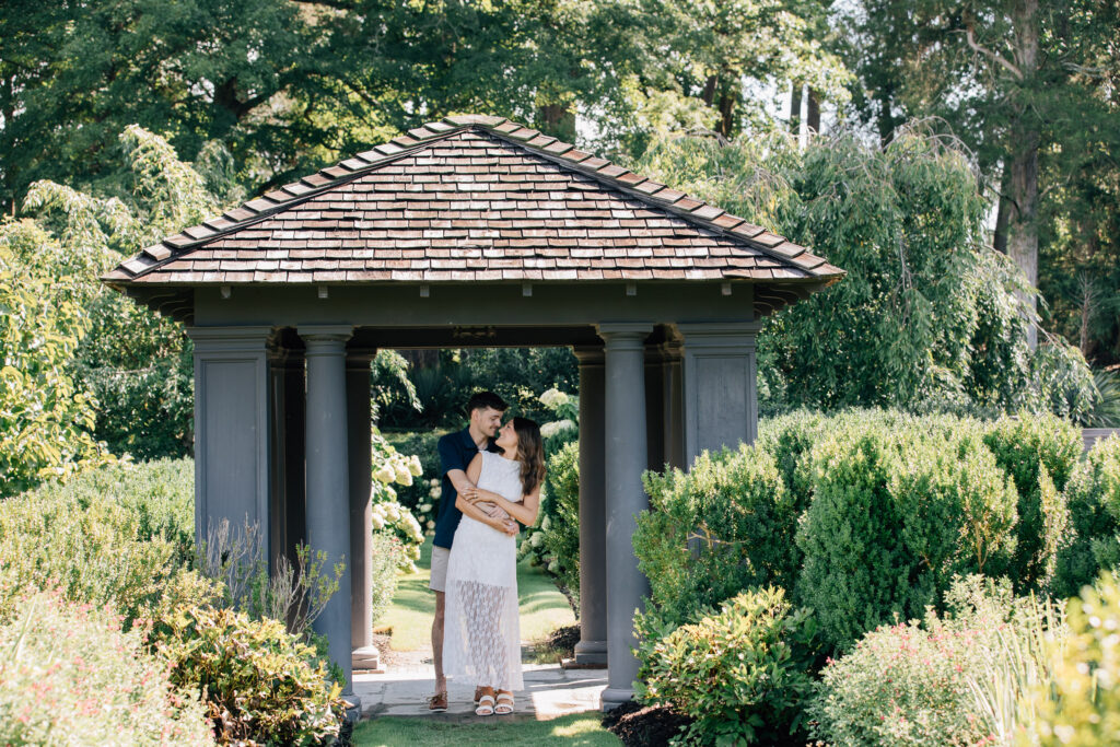 couple hugs under a gazebo at reynolda gardens during their engagement session