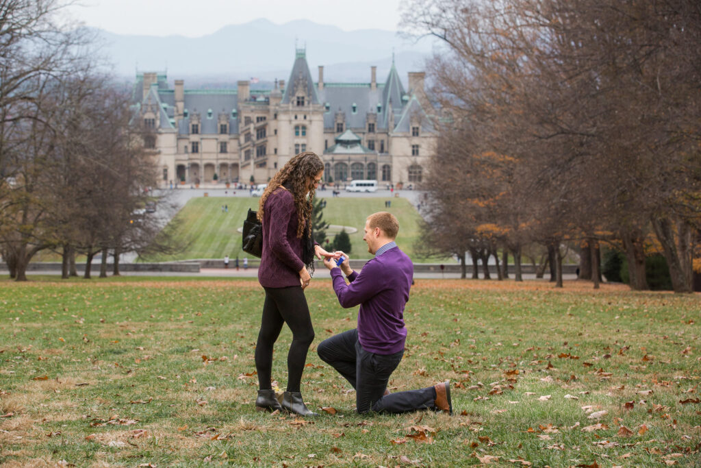 a man proposes on one knee and slips a ring on his partner's finger at the statue of the diana at biltmore estate