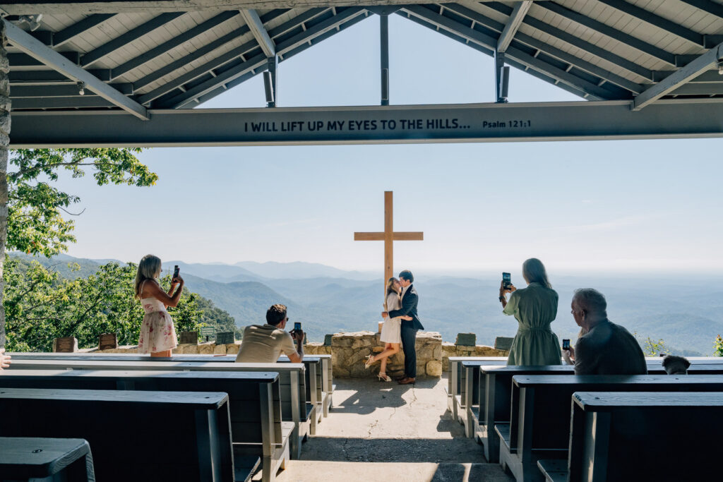 family members watch and photograph a newly engaged couple during their surprise proposal at pretty place chapel in sc