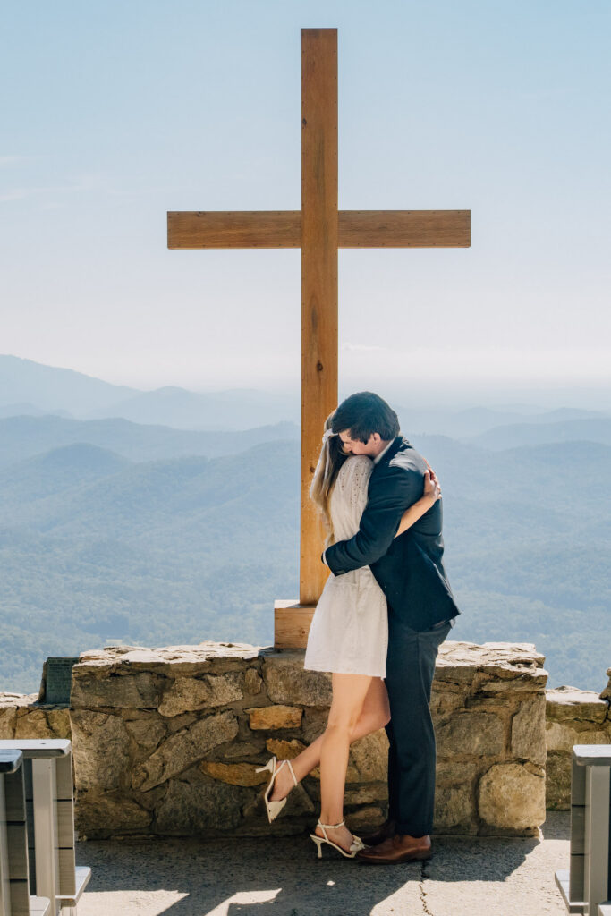 a couple embraces in front of a big cross during their surprise proposal