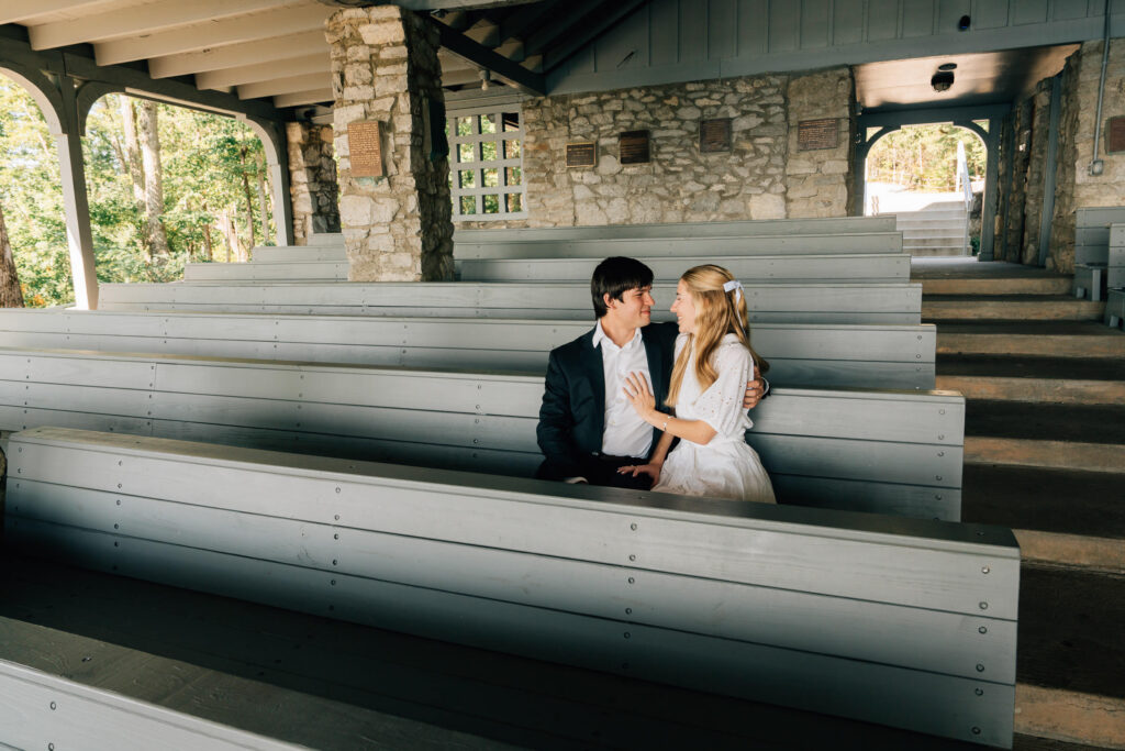 couple sits together on the pews of pretty place chapel and celebrates their engagement